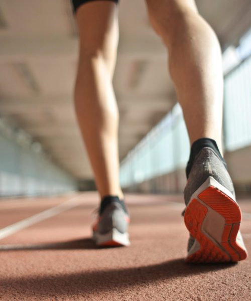 Back view of a runner's legs in a stadium, focusing on footwear and athletic motion.