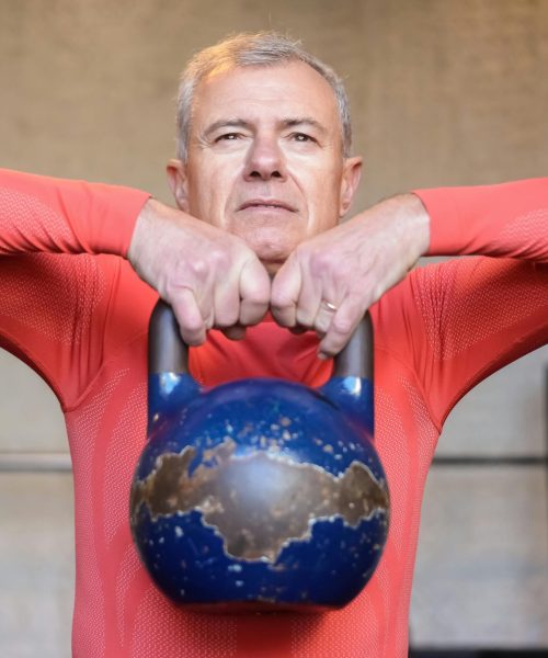 Senior man performing kettlebell exercises indoors, showcasing strength and healthy living.
